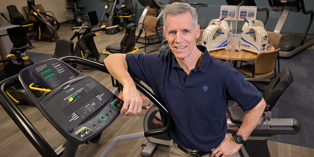 John Roche stands in fromt of a cardiac rehab machine..